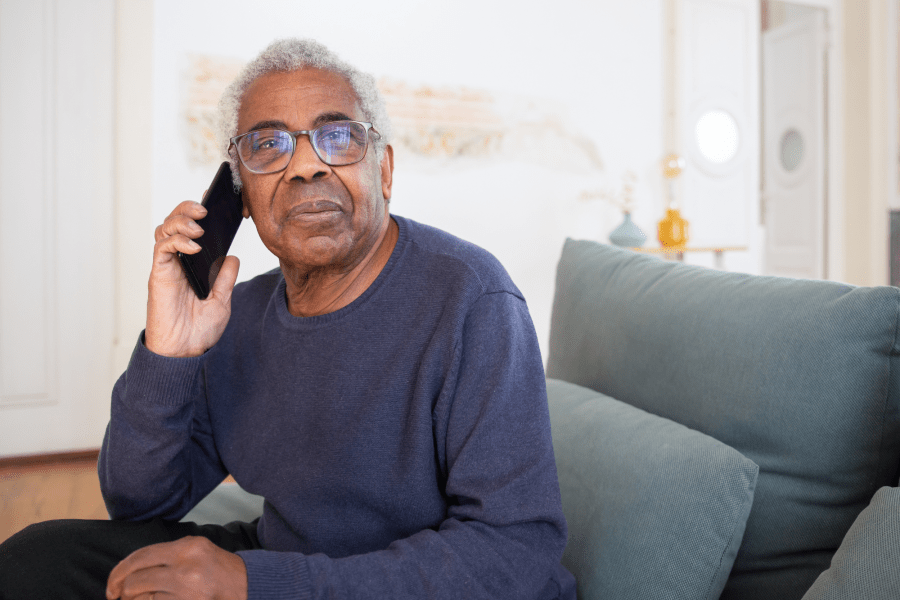 An adult sitting on a couch with a phone to their ear.