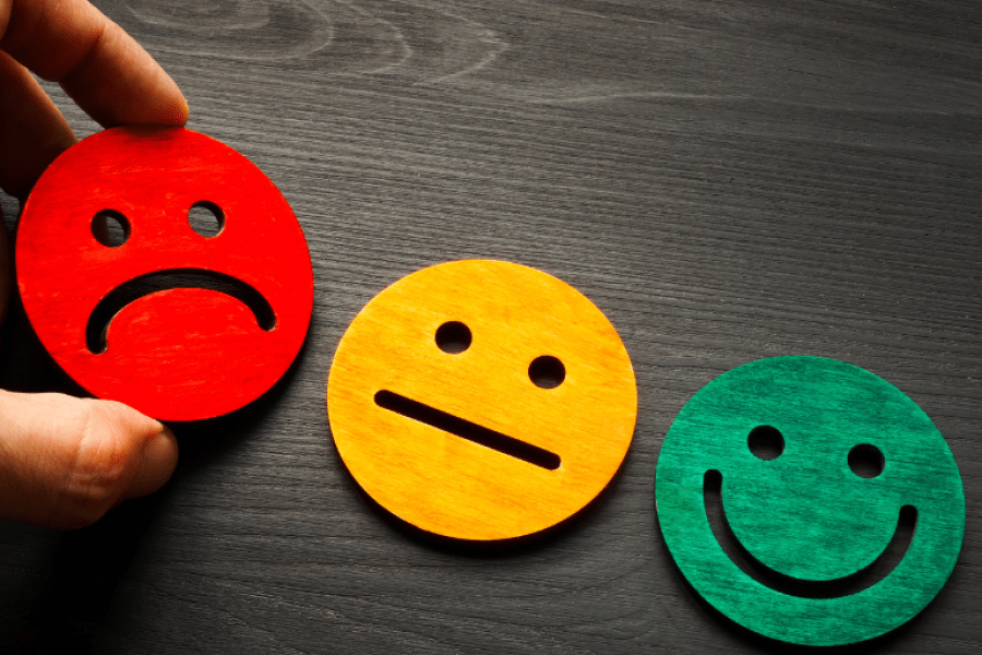 A hand arranging three face icons (red sad face, yellow neutral face, green happy face)