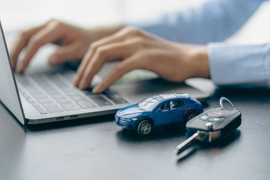 Hands typing on a keyboard with a toy car and car keys next to it