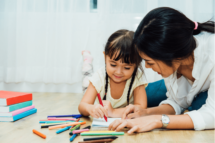 An adult and an infant laying on the ground. The infant is drawing.